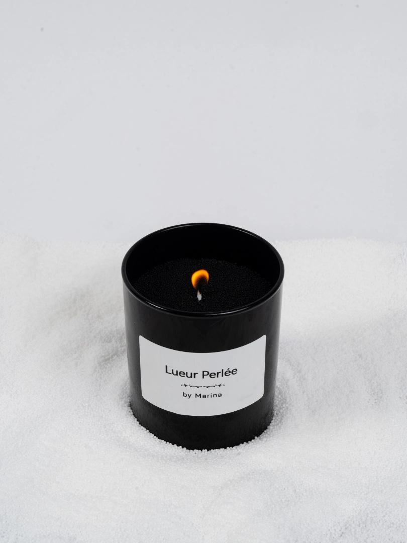 Bougie Lueur Perlée allumée dans un contenant en verre noir.