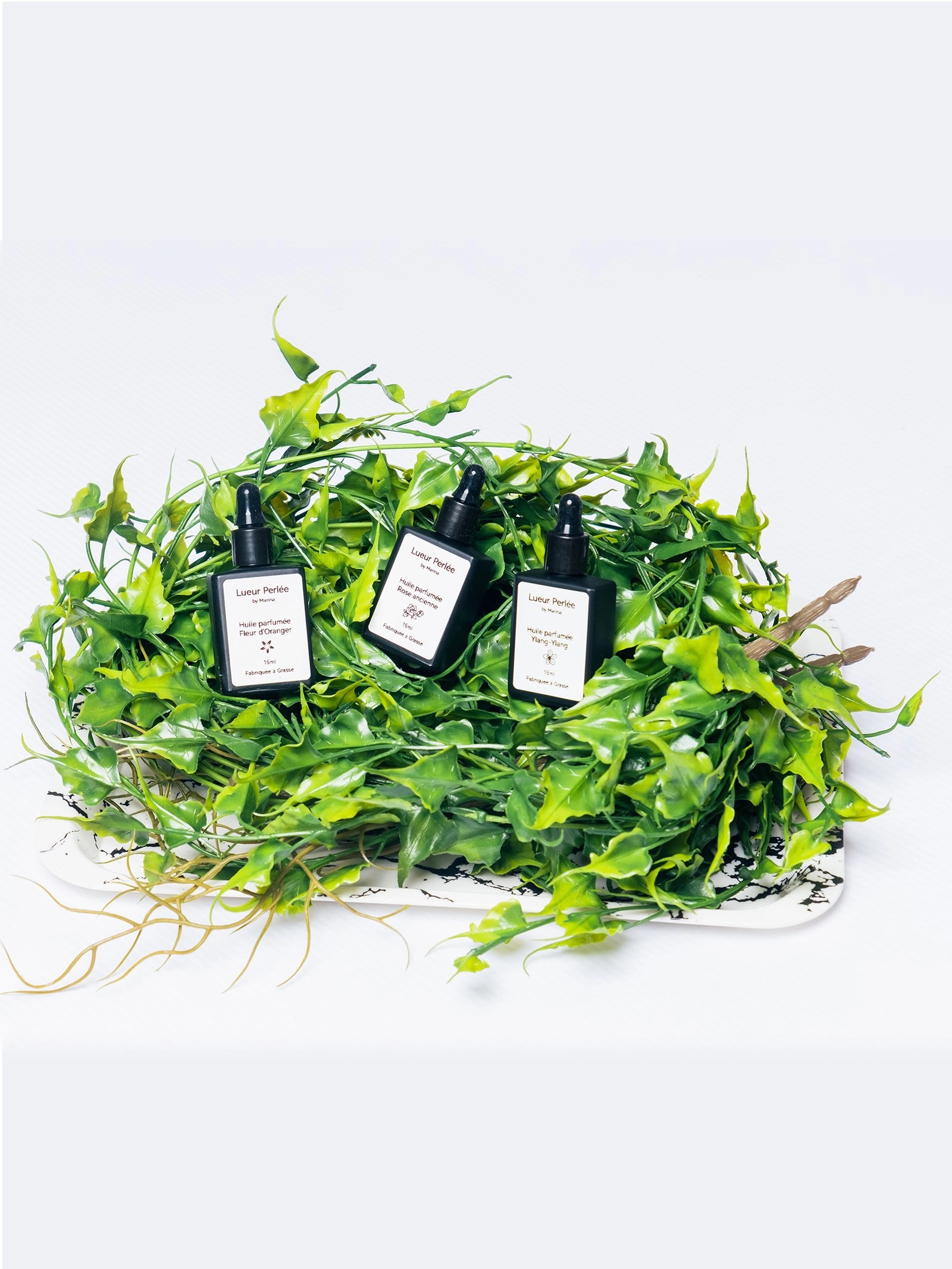 Huile parfumée pour bougie perlée sur un lit de feuilles vertes.