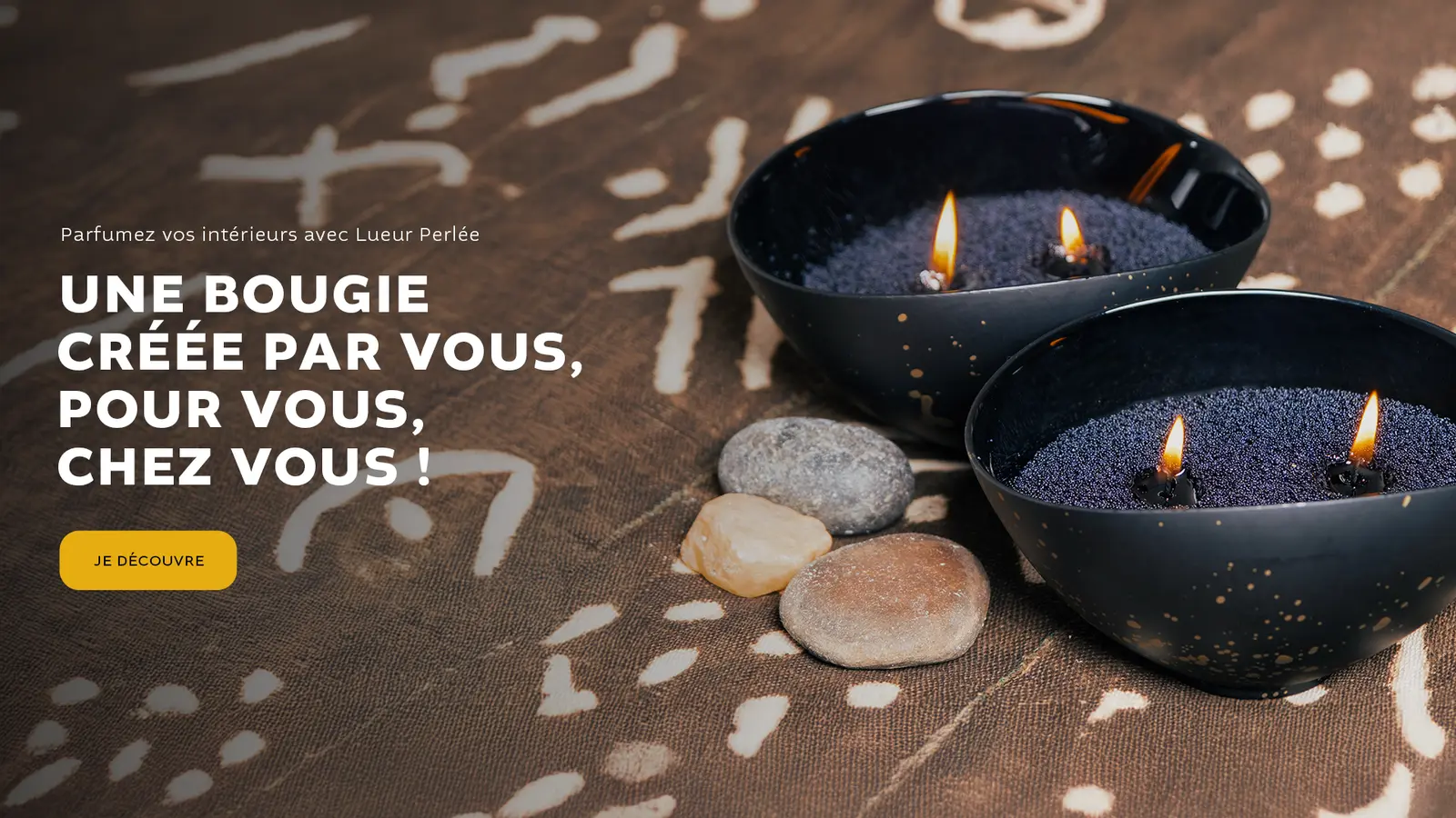 Deux bougies Lueur Perlée allumées sur un tissu africain.